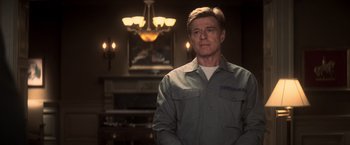Movie still from “The Last Castle” (2001), directed by Rod Lurie – A man standing in front of a fireplace in front of a chandelier; Medium shot, Over the shoulder angle