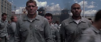 Movie still from “The Last Castle” (2001), directed by Rod Lurie – A group of men standing next to each other in front of smoke stacks; Medium shot, Low angle