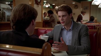 Movie still from “The Last Days of Disco” (1998), directed by Whit Stillman – Two men are sitting at a table and one is holding a coffee cup; Medium shot, Over the shoulder angle