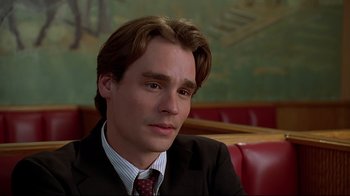 Movie still from “The Last Days of Disco” (1998), directed by Whit Stillman – A man in a suit and tie sitting in a restaurant booth; Close Up shot, High angle