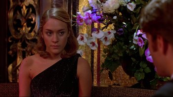 Movie still from “The Last Days of Disco” (1998), directed by Whit Stillman – A woman sitting in front of a flower arrangement on a couch; Close Up shot, Over the shoulder angle
