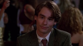 Movie still from “The Last Days of Disco” (1998), directed by Whit Stillman – A man in a suit and tie sitting in front of a group of people; Close Up shot, Over the shoulder angle