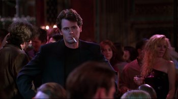Movie still from “The Last Days of Disco” (1998), directed by Whit Stillman – A man smoking a cigarette in front of a group of people; Medium shot, Over the shoulder angle