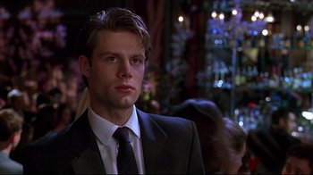 Movie still from “The Last Days of Disco” (1998), directed by Whit Stillman – A man in a suit and tie in front of a crowd; Close Up shot, Over the shoulder angle