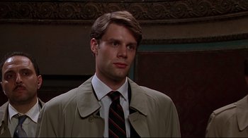 Movie still from “The Last Days of Disco” (1998), directed by Whit Stillman – A man wearing a suit and tie standing in front of a wall; Close Up shot, Low angle