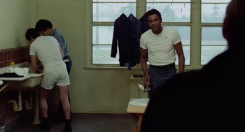 Movie still from “The Last Detail” (1973), directed by Hal Ashby – A man in white shirt and blue shorts standing in a room; Medium shot, Over the shoulder angle