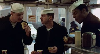 Two men in white hats eating hot dogs in front of a window