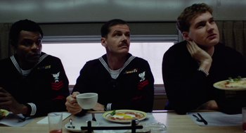 Movie still from “The Last Detail” (1973), directed by Hal Ashby – A man sitting in front of a plate of food and a cup; Medium shot, Low angle