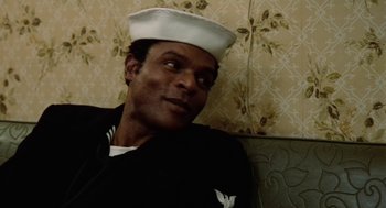 Movie still from “The Last Detail” (1973), directed by Hal Ashby – A man wearing a sailor's hat sitting on a couch; Close Up shot, Over the shoulder angle