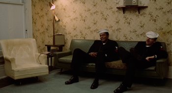 Movie still from “The Last Detail” (1973), directed by Hal Ashby – A man sitting on top of a couch in a living room; Wide shot, High angle