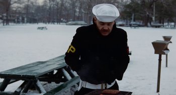 Movie still from “The Last Detail” (1973), directed by Hal Ashby – A man in a uniform standing next to a grill in the snow; Medium shot, Over the shoulder angle