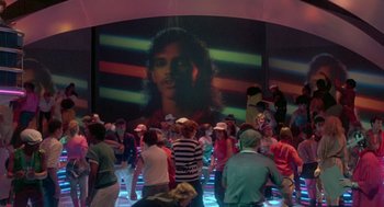 Movie still from “The Last Dragon” (1985), directed by Michael Schultz – A group of people standing in front of a large screen; Wide shot, High angle