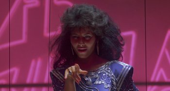 Movie still from “The Last Dragon” (1985), directed by Michael Schultz – A woman in a purple dress with long black curly hair; Close Up shot, Low angle