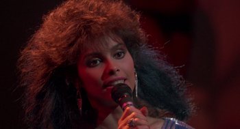 Movie still from “The Last Dragon” (1985), directed by Michael Schultz – A woman is holding a microphone up to her face; Close Up shot, High angle