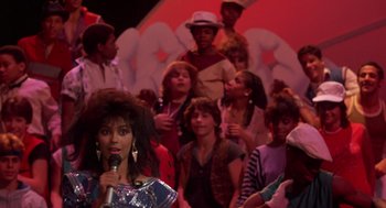 Movie still from “The Last Dragon” (1985), directed by Michael Schultz – A group of people standing in front of a microphone; Medium shot, Over the shoulder angle