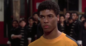 Movie still from “The Last Dragon” (1985), directed by Michael Schultz – A man in a yellow shirt is in front of a group of people; Close Up shot, Low angle