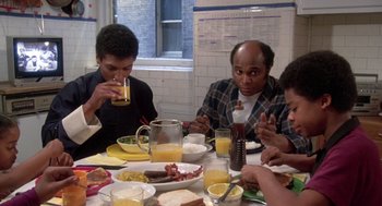 Movie still from “The Last Dragon” (1985), directed by Michael Schultz – A group of people sitting at a table with plates of food; Medium shot, High angle