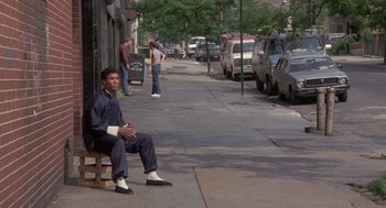 Movie still from “The Last Dragon” (1985), directed by Michael Schultz – A man sitting on top of a wooden bench on a sidewalk; Wide shot, Low angle