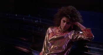 Movie still from “The Last Dragon” (1985), directed by Michael Schultz – A woman in a gold and red shirt is posing for a picture; Medium shot, Low angle