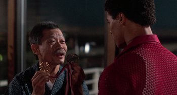 Movie still from “The Last Dragon” (1985), directed by Michael Schultz – A man is holding a medal in front of another man; Close Up shot, Over the shoulder angle