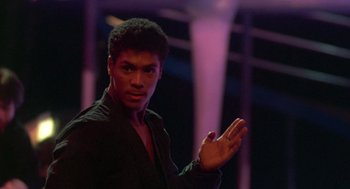 Movie still from “The Last Dragon” (1985), directed by Michael Schultz – A man in a black shirt is holding his hands out; Medium shot, Low angle
