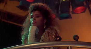 Movie still from “The Last Dragon” (1985), directed by Michael Schultz – A woman sitting in a chair with her hand on her chin; Close Up shot, Low angle