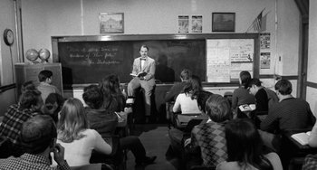 Movie still from “The Last Picture Show” (1971), directed by Peter Bogdanovich – Black and white photograph of a man sitting in front of a chalkboard; Wide shot, High angle