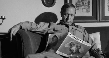 Movie still from “The Last Picture Show” (1971), directed by Peter Bogdanovich – A black and white photo of a man sitting on a couch reading a magazine; Close Up shot, Over the shoulder angle