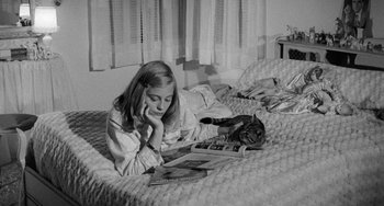 Movie still from “The Last Picture Show” (1971), directed by Peter Bogdanovich – A woman laying on a bed reading a magazine; Medium shot, High angle