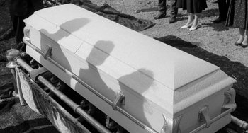 Movie still from “The Last Picture Show” (1971), directed by Peter Bogdanovich – Two people standing in front of a casket in black and white; Medium shot, Over the shoulder angle