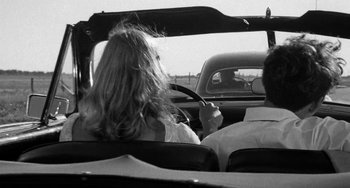 Movie still from “The Last Picture Show” (1971), directed by Peter Bogdanovich – A woman sitting in the passenger seat of a car while holding a steering wheel; Medium shot, Over the shoulder angle