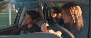 Movie still from “The Last Song” (2010), directed by Julie Anne Robinson – Three people sitting in a car with one of them holding a steering wheel; Medium shot, Over the shoulder angle