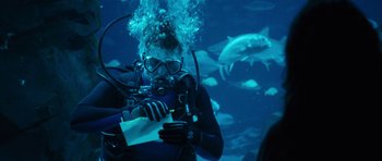Movie still from “The Last Song” (2010), directed by Julie Anne Robinson – A man in a wet suit is holding a piece of paper in front of a group of sharks; Medium shot, Over the shoulder angle