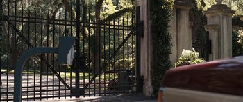 Movie still from “The Last Song” (2010), directed by Julie Anne Robinson – A black cat sitting on the ground behind a metal gate; Wide shot, Over the shoulder angle