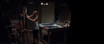 Movie still from “The Last Song” (2010), directed by Julie Anne Robinson – A woman standing next to a work bench in a dark room; Wide shot, High angle