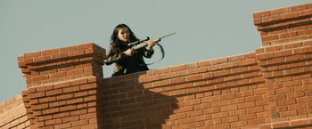 Movie still from “The Last Stand” (2013), directed by Jee-woon Kim – A woman is holding a rifle on top of a brick wall; Medium shot, Low angle
