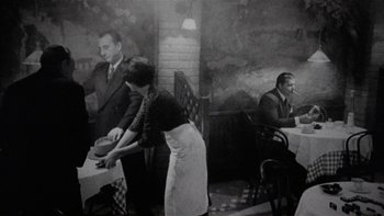 Movie still from “The Last Tycoon” (1976), directed by Elia Kazan – An old black and white photo of a man and a woman at a table; Wide shot, High angle