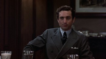 Movie still from “The Last Tycoon” (1976), directed by Elia Kazan – A man wearing a suit and tie sitting at a table with two glasses; Close Up shot, Over the shoulder angle