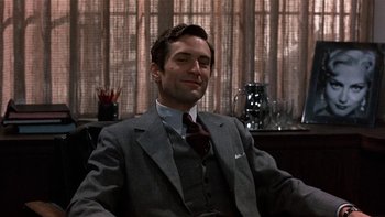 Movie still from “The Last Tycoon” (1976), directed by Elia Kazan – A man sitting in a chair wearing a suit and tie; Close Up shot, Low angle
