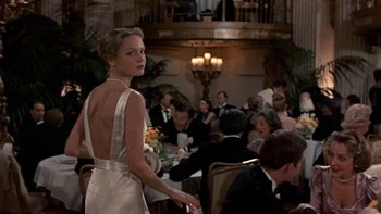 Movie still from “The Last Tycoon” (1976), directed by Elia Kazan – A woman in a white dress standing in front of a group of people; Medium shot, Over the shoulder angle