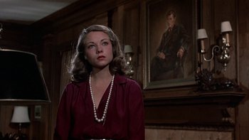 Movie still from “The Last Tycoon” (1976), directed by Elia Kazan – A woman wearing a red shirt and pearls standing in front of a painting; Medium shot, Low angle