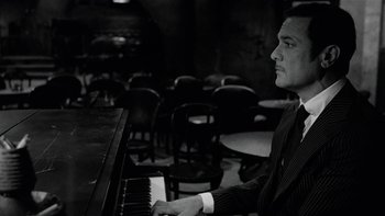 Movie still from “The Last Tycoon” (1976), directed by Elia Kazan – A man sitting at a piano in front of a bunch of chairs; Medium shot, Low angle