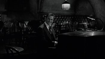 Movie still from “The Last Tycoon” (1976), directed by Elia Kazan – A man in a suit sitting at a piano in a restaurant; Medium shot, Over the shoulder angle