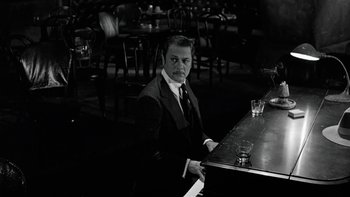 Movie still from “The Last Tycoon” (1976), directed by Elia Kazan – A man sitting at a bar in front of two glasses of wine; Medium shot, High angle