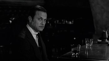 Movie still from “The Last Tycoon” (1976), directed by Elia Kazan – A black and white photo of a man sitting at a table; Close Up shot, Over the shoulder angle