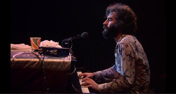 Movie still from “The Last Waltz” (1978), directed by Martin Scorsese – A man sitting at a piano in front of microphones; Medium shot, Low angle