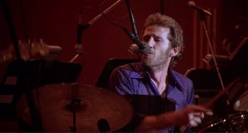 Movie still from “The Last Waltz” (1978), directed by Martin Scorsese – A man with a microphone on his head playing drums; Close Up shot, Low angle