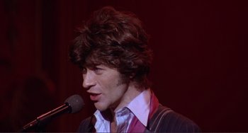 Movie still from “The Last Waltz” (1978), directed by Martin Scorsese – A man in a suit is speaking into a microphone; Close Up shot, Low angle