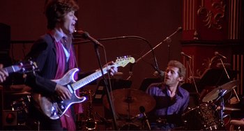 Movie still from “The Last Waltz” (1978), directed by Martin Scorsese – A man sitting next to another man holding a guitar; Medium shot, Low angle