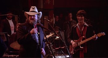 Movie still from “The Last Waltz” (1978), directed by Martin Scorsese – A man in a cowboy hat is playing a guitar; Medium shot, Over the shoulder angle